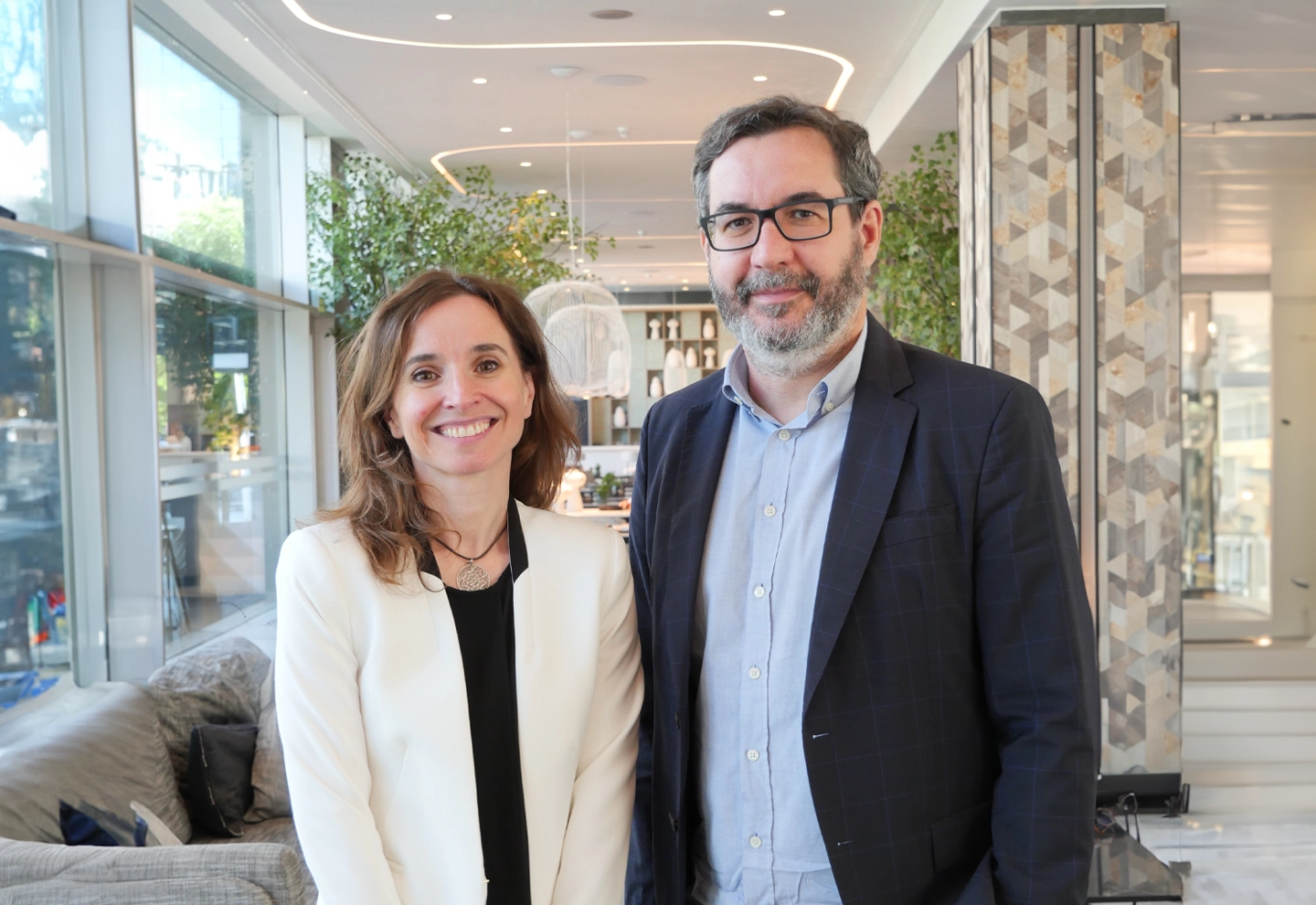 Teresa Zamora Garcia y Jorge Barrero. Posan sonrientes ante la cámara, en el hall de ILUNION Atrium