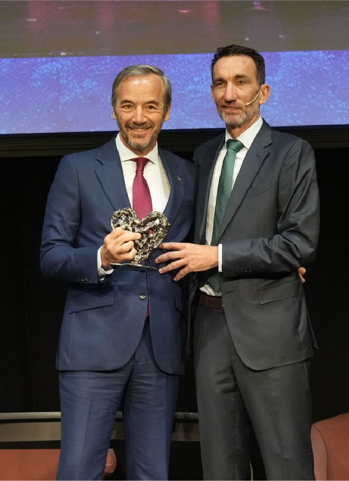 Nuestro CEO, José Ángel Preciados, recibe un reconocimiento de manos del director de Hosteltur, Manuel Molina. Ambos están sobre un escenario y se encuentran delante de una pantalla y de dos sillones.